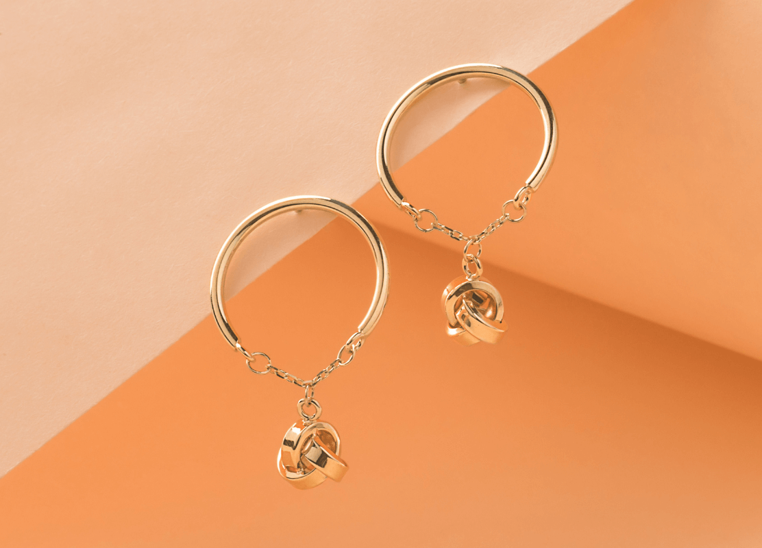 Dvije zlatne alke naušnice s privjeskom u obliku čvora koji vise na svakoj, dodajući dašak elegancije i romantike.